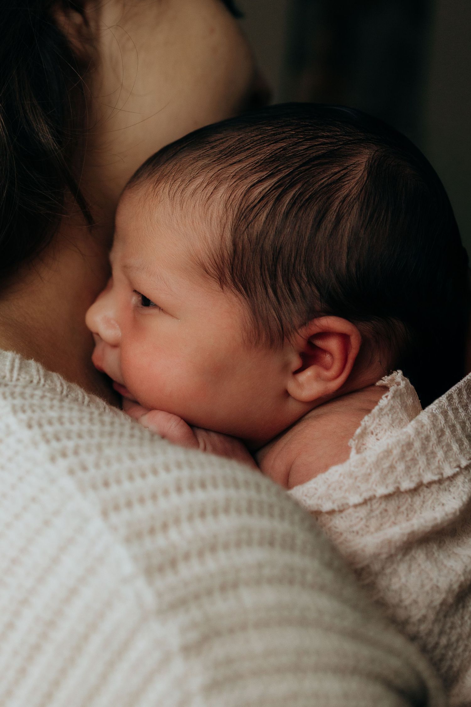 Close-up of sleeping newborn baby wrapped in soft white knit blanket.