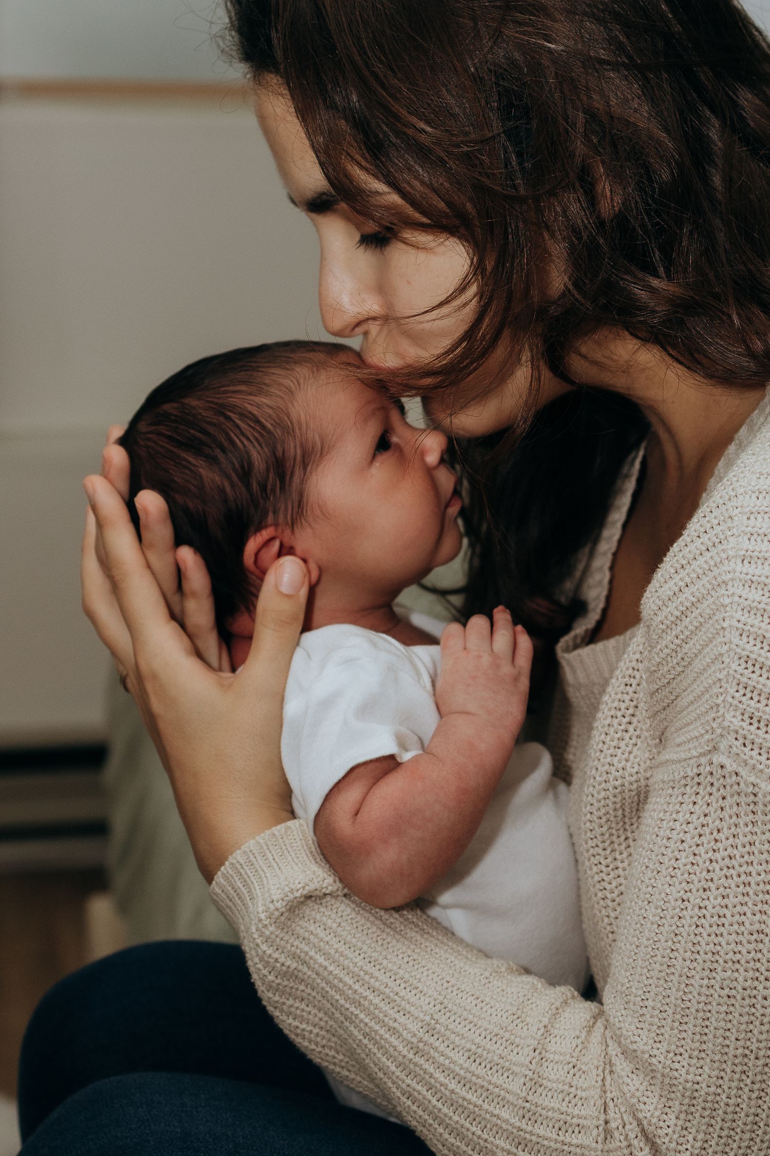 Sweet nurturing moment between parent and newborn in cream sweater.