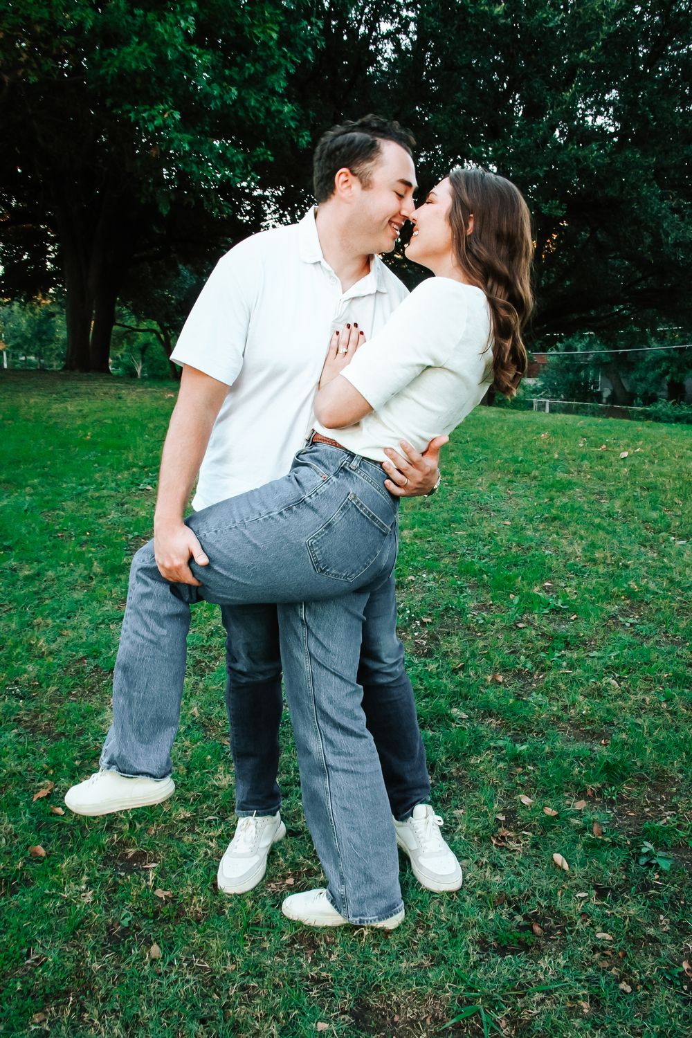 Couple sharing a kiss outdoors on green grass, man lifting woman slightly in a romantic embrace.