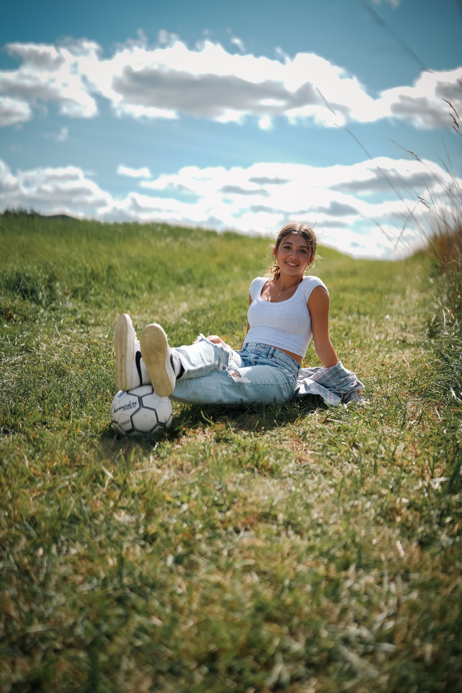 Athletic lifestyle photo shoot on a grassy hillside with a soccer ball on a sunny day.