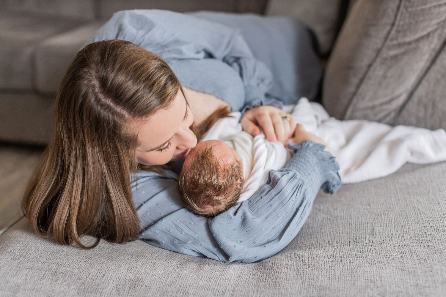 A tender moment between parent and newborn baby while cuddling on a grey couch.
