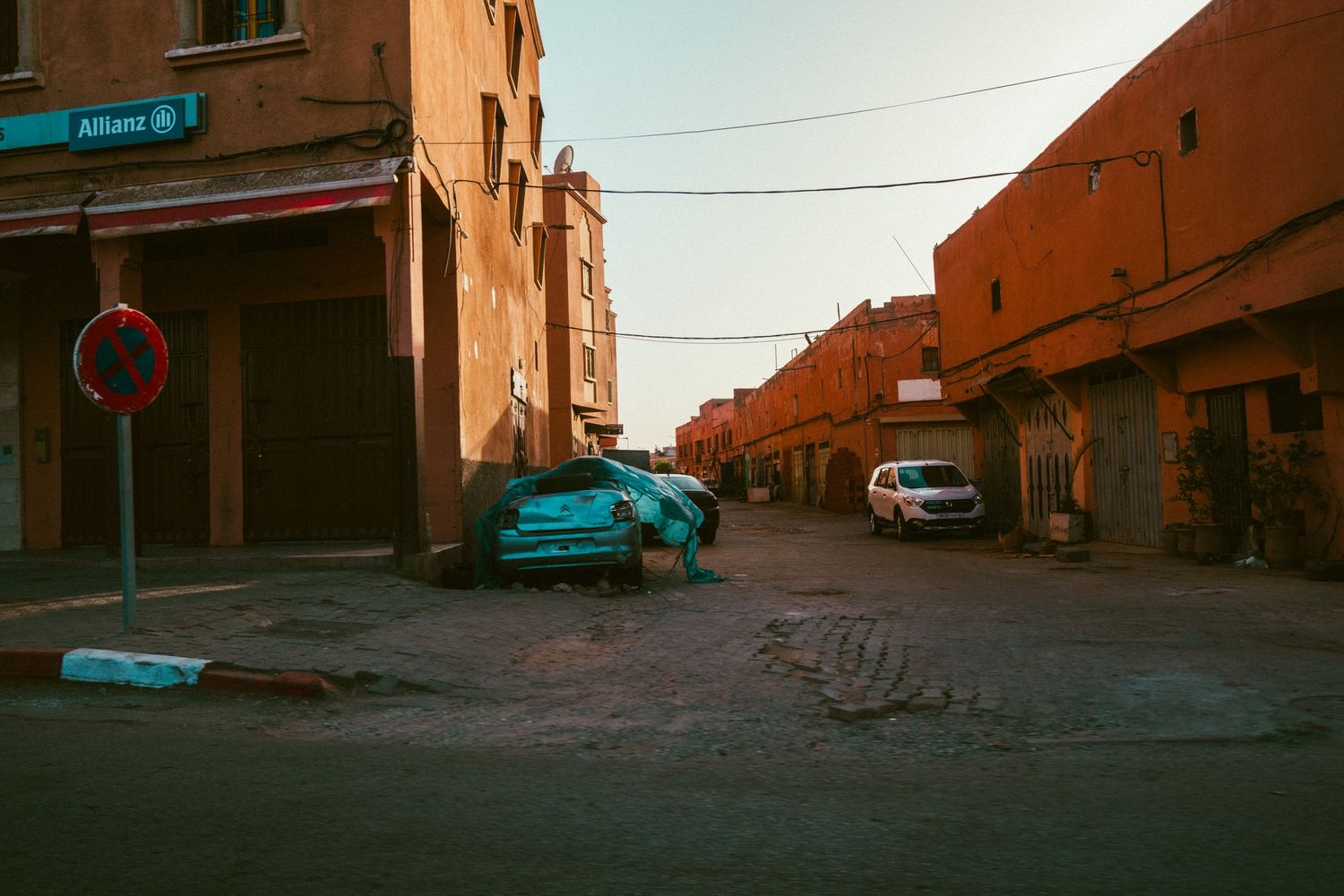 Vintage blue car parked on a cobblestone street corner in Morocco with orange buildings and warm sunset lighting.