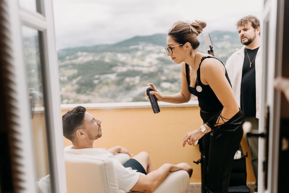 Casual hangout scene on balcony with mountains in background as people converse over drinks.