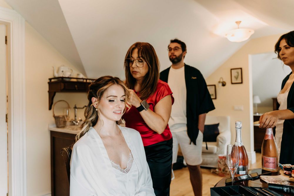 Wedding preparations underway as someone gets their hair styled in a white robe while others assist in a bright room.