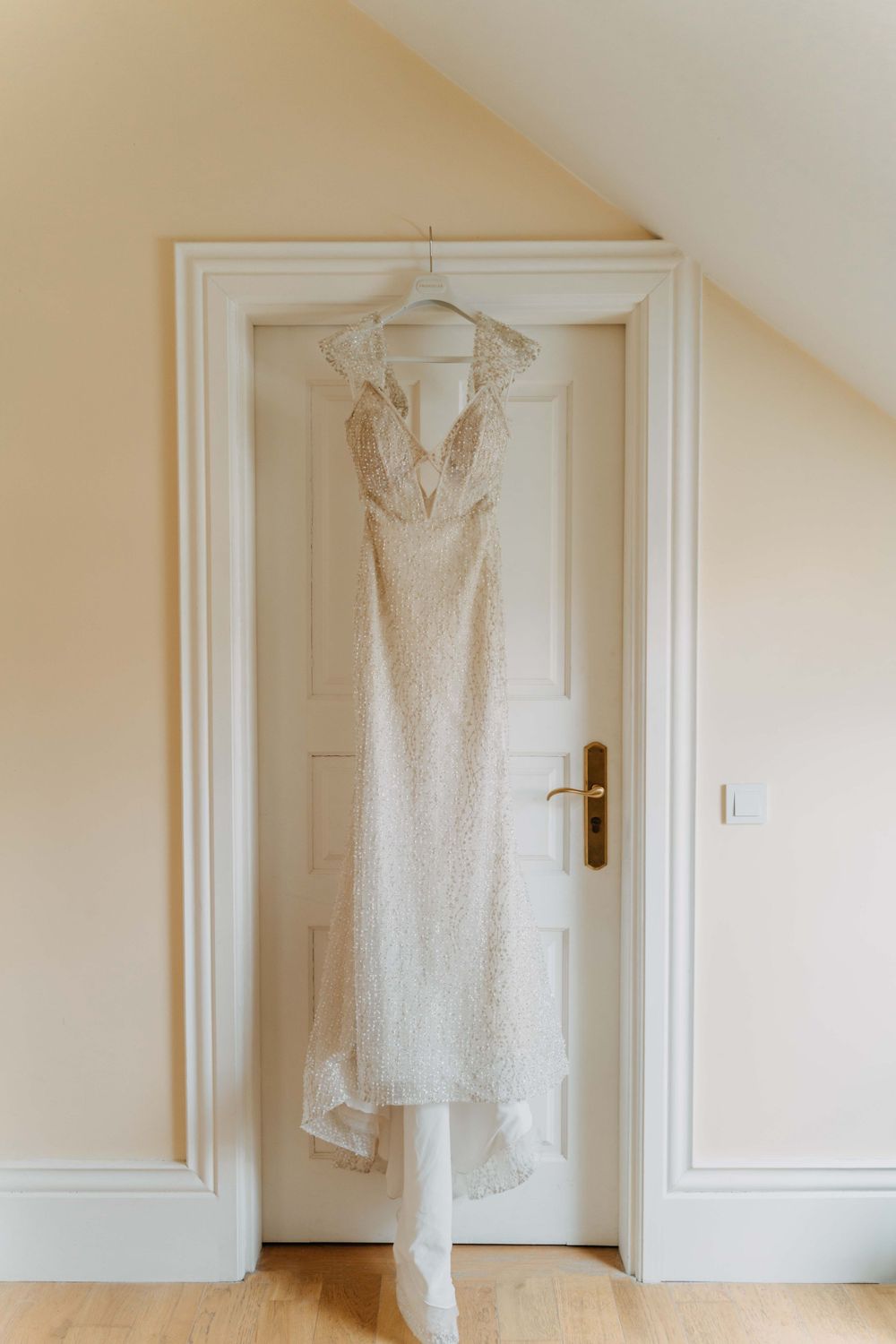 A delicate white lace wedding dress with halter neckline hangs elegantly on a white wooden door.