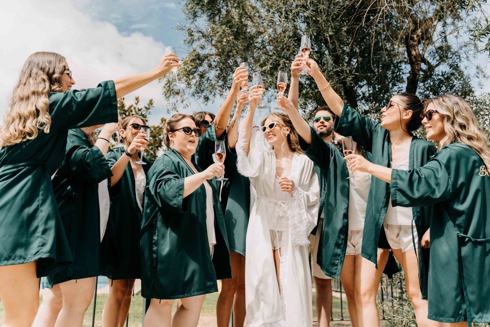 Wedding party in emerald green robes celebrates with a champagne toast under sunny skies outdoors.