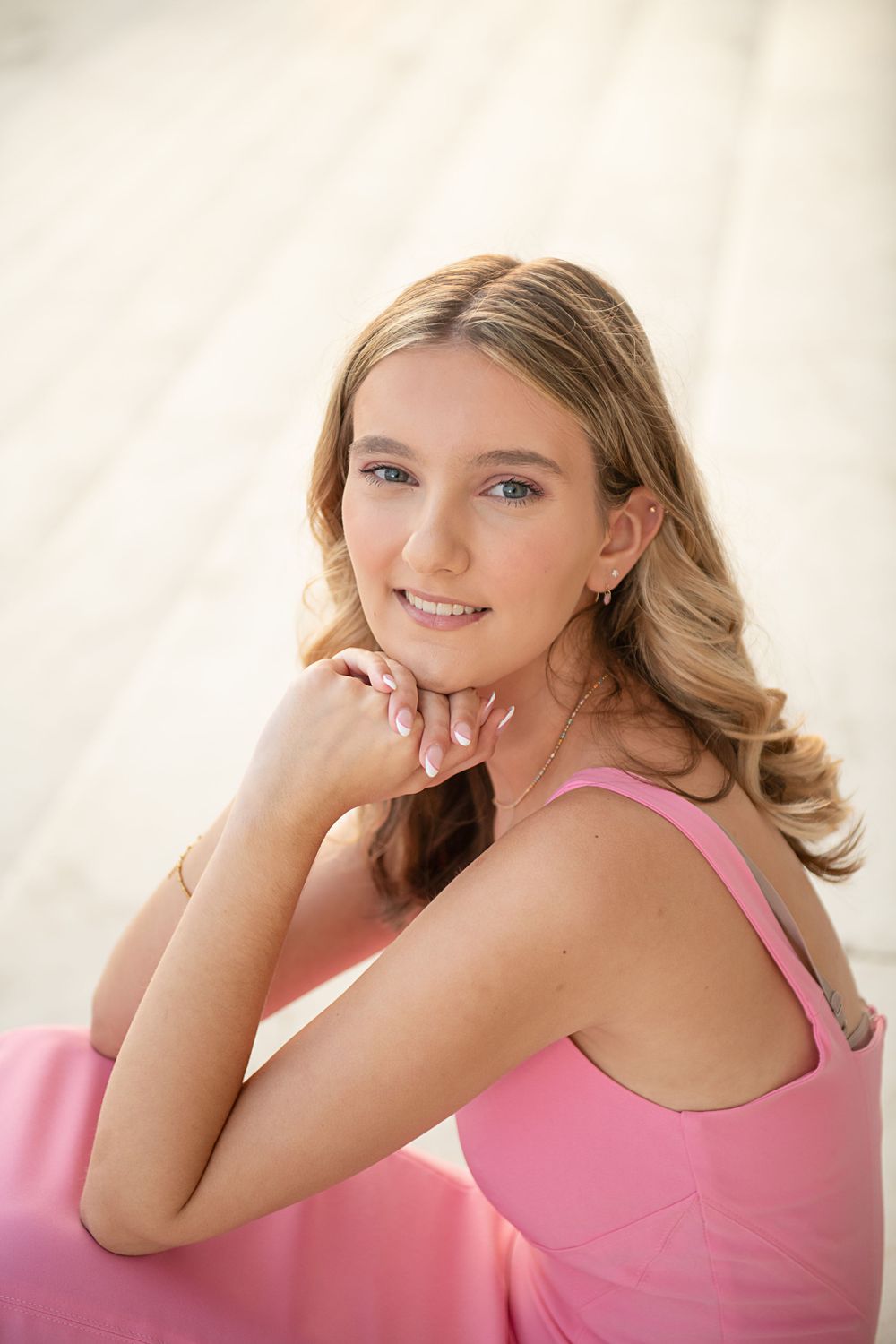 Portrait of young woman in pink tank top against light backdrop.