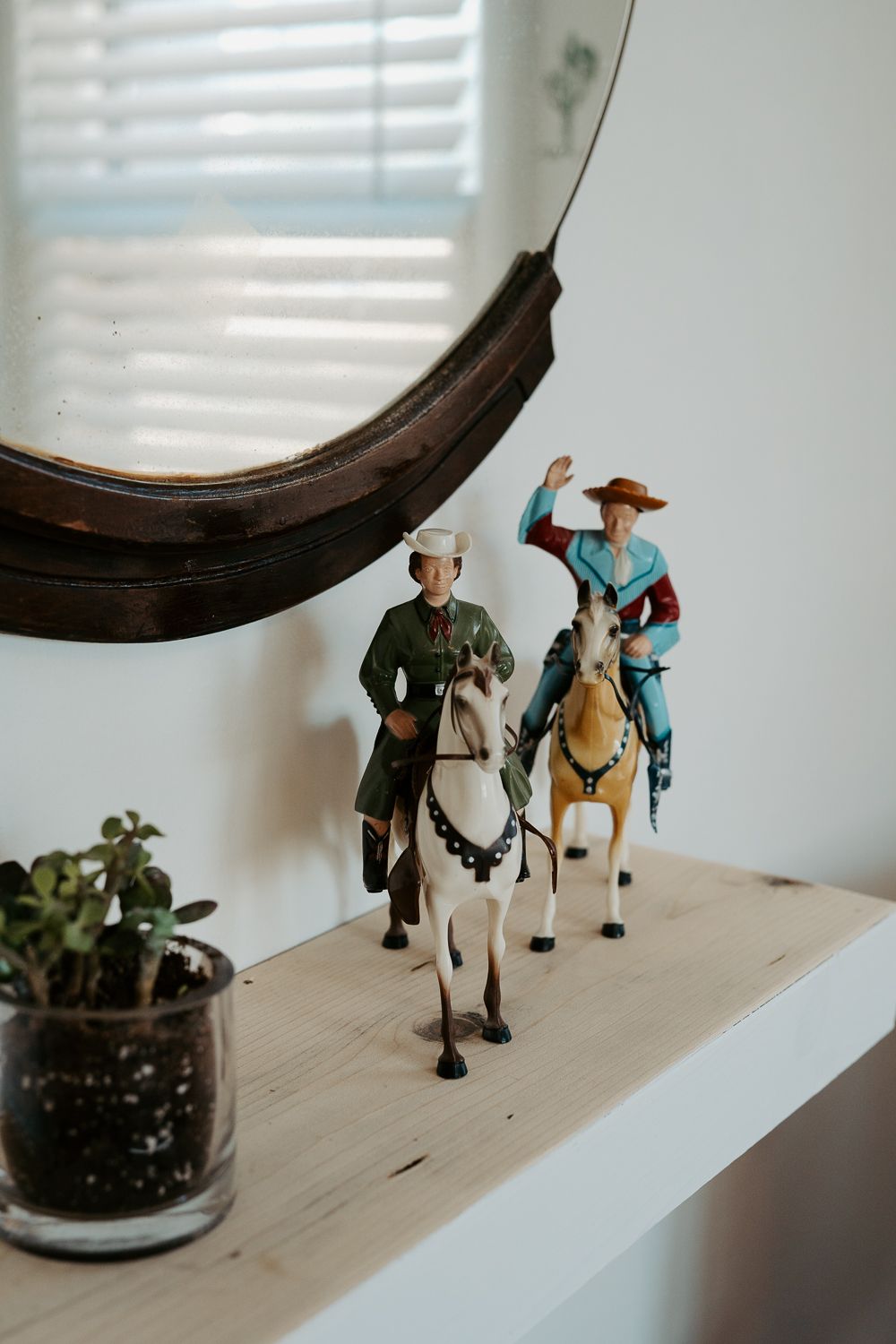 Small figurines of people and horses displayed on a white shelf near a window.