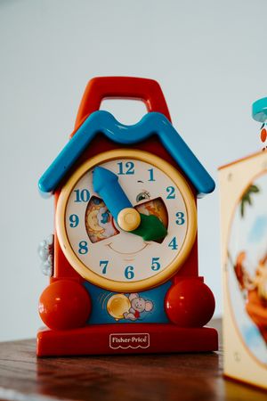 Vintage Fisher-Price toy clock with blue roof and red sides on wooden surface.