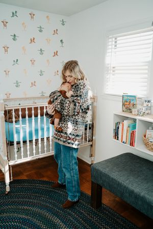 A child's bedroom features white furniture, patterned wallpaper, and a braided rug on hardwood floors.