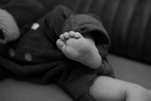 Black and white photograph of small feet against dark fabric creating contrast.