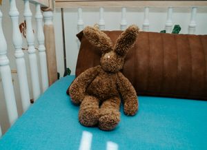Brown teddy bear resting on turquoise carpet next to white railing.