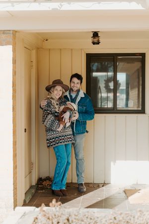 Couple standing in doorway of white house with blue accents.