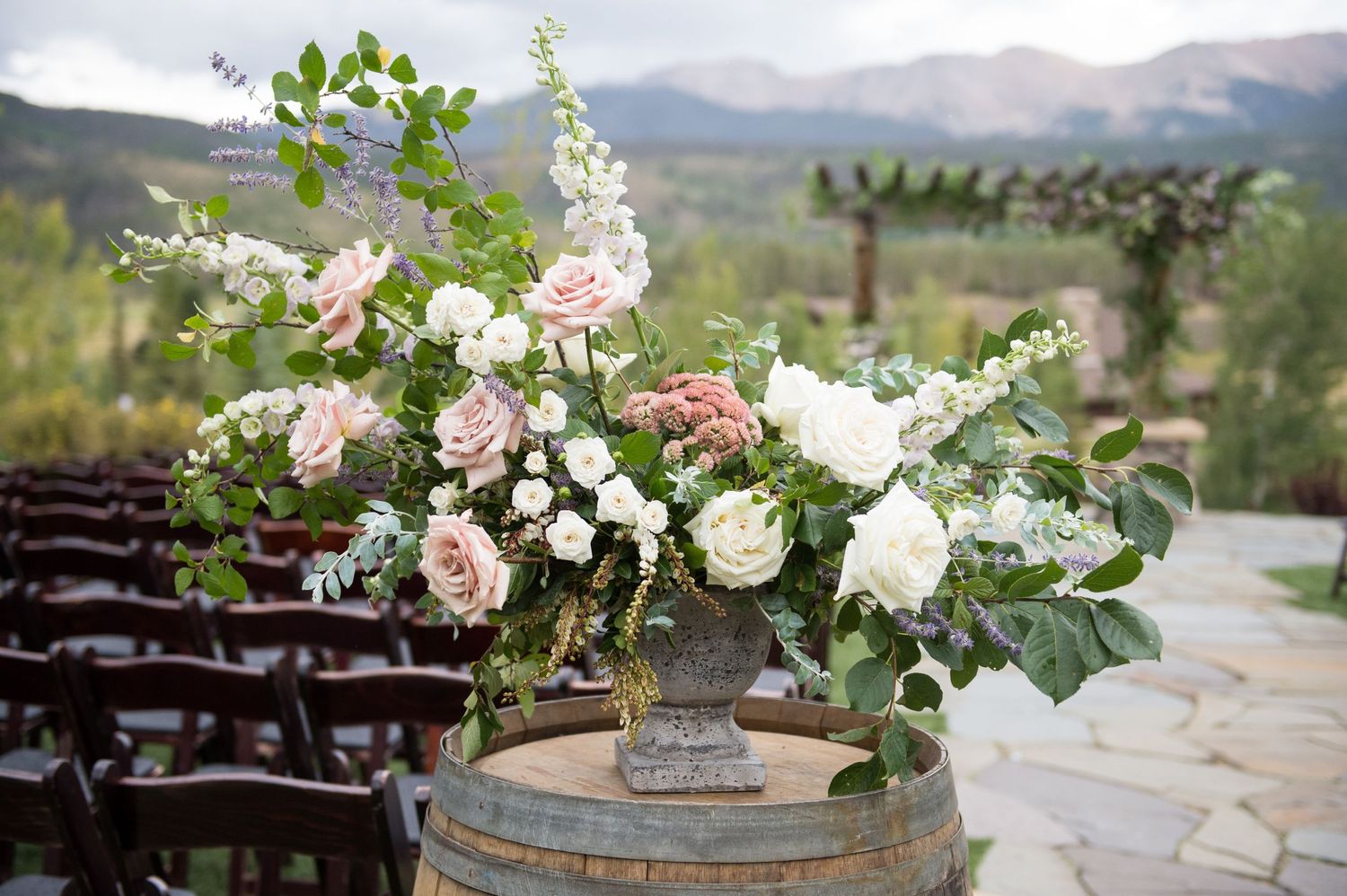 Elegant floral arrangement with pink and white roses on a rustic wine barrel.