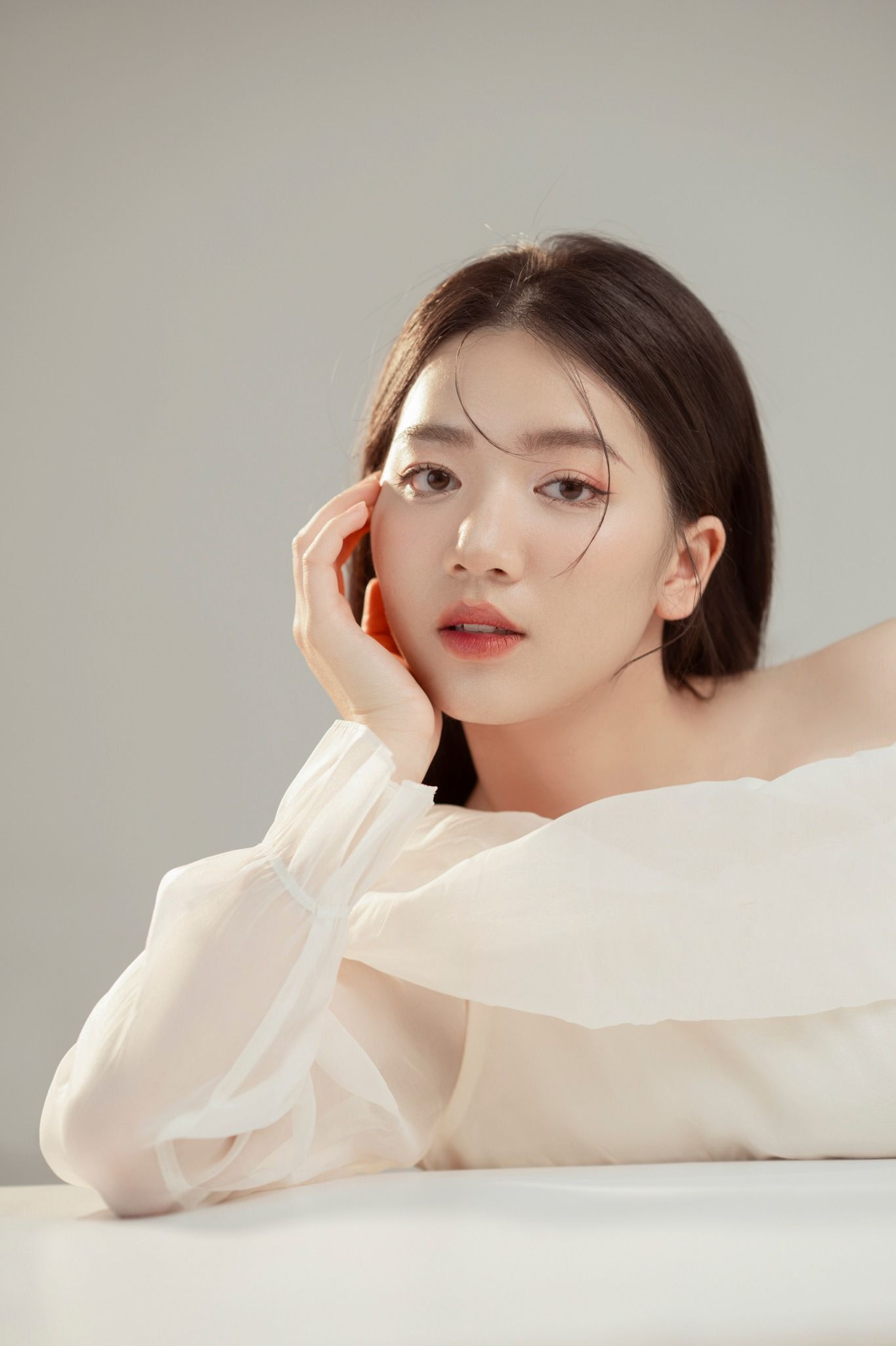 Modern beauty portrait with minimalist styling and soft lighting against gray backdrop.