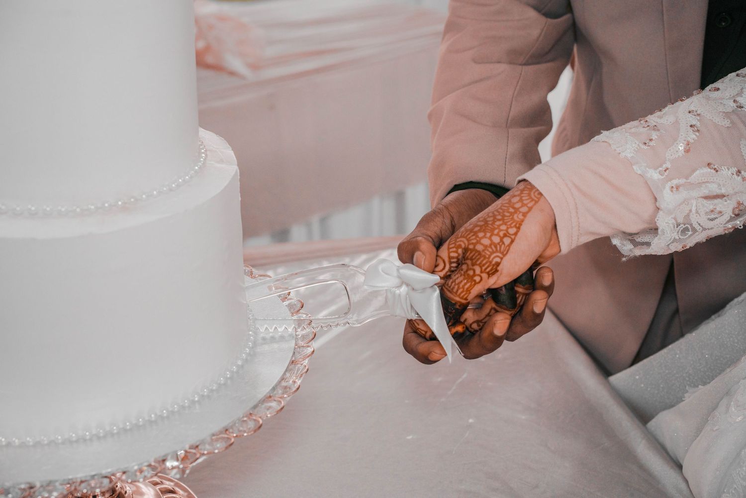 Close-up of hands cutting a white wedding cake with elegant details.
