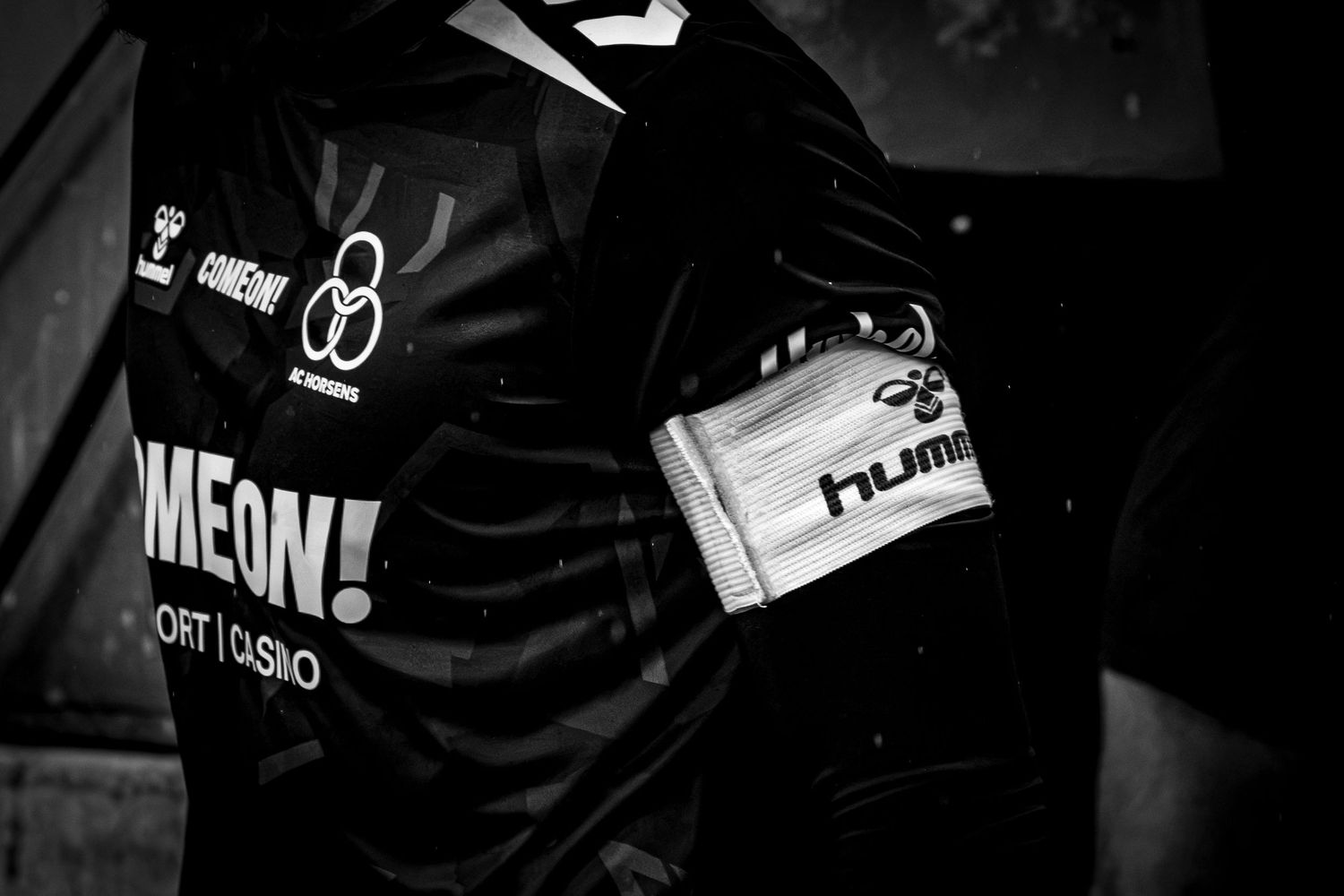 Black and white close-up of a Hummel sports jersey with captain armband and GAMEON sponsor logo.