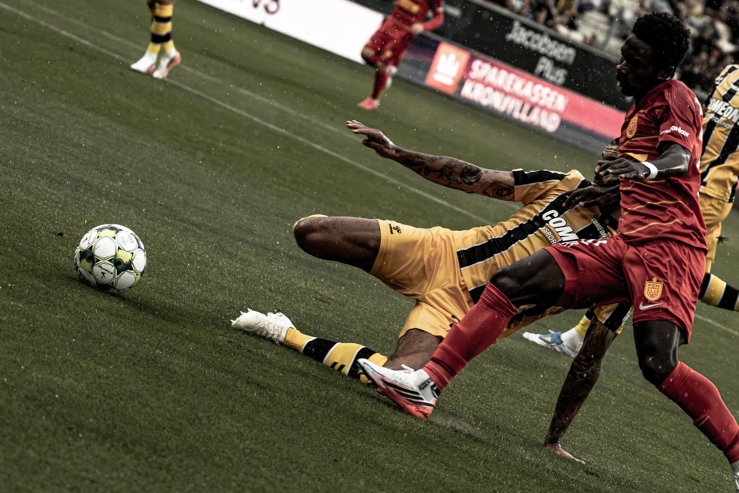 Two soccer players battle for the ball during an intense sliding tackle in a professional match.