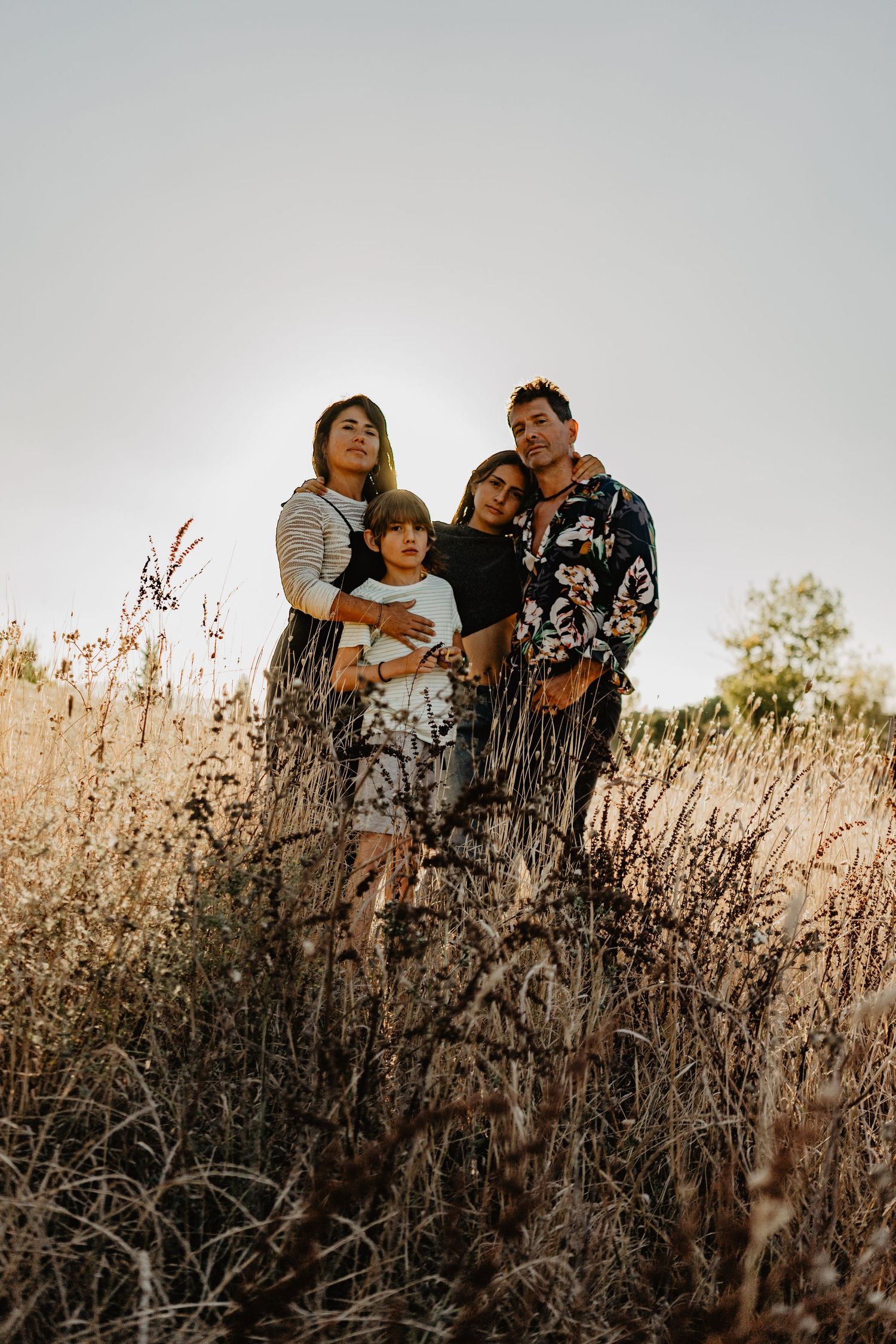 Família unida em campo dourado ao pôr do sol, expressando amor, conexão e tranquilidade em meio à natureza.