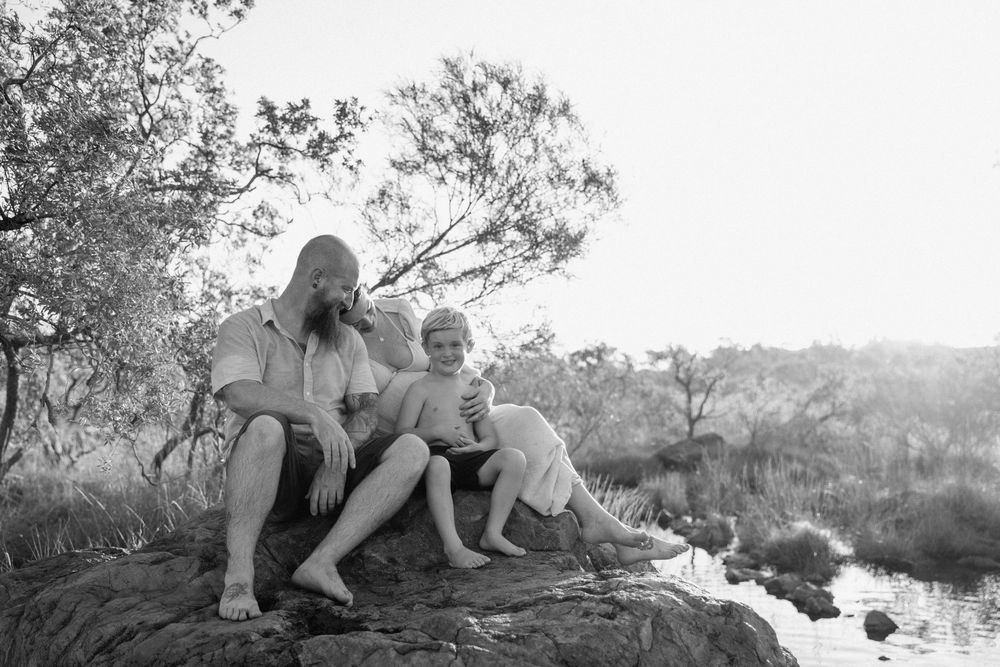 A serene black and white photograph shows people sitting together on a rocky outcrop overlooking a tranquil water scene.