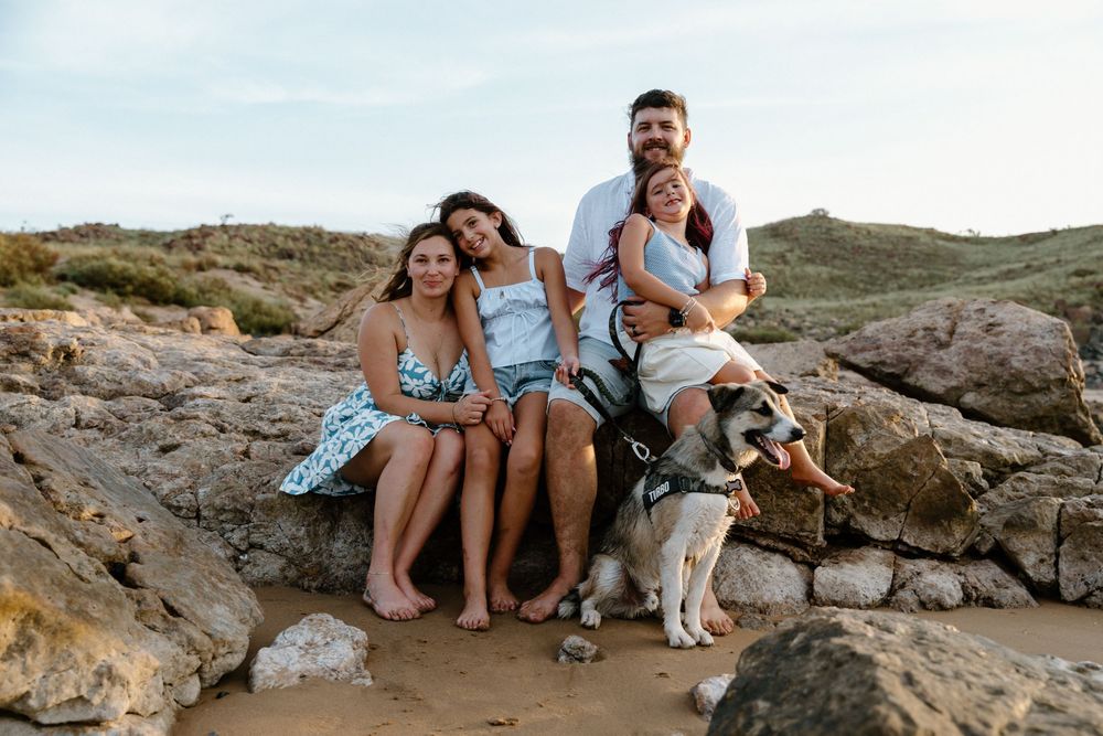 A group sits together with their dog on coastal rocks during a sunny day at the beach.