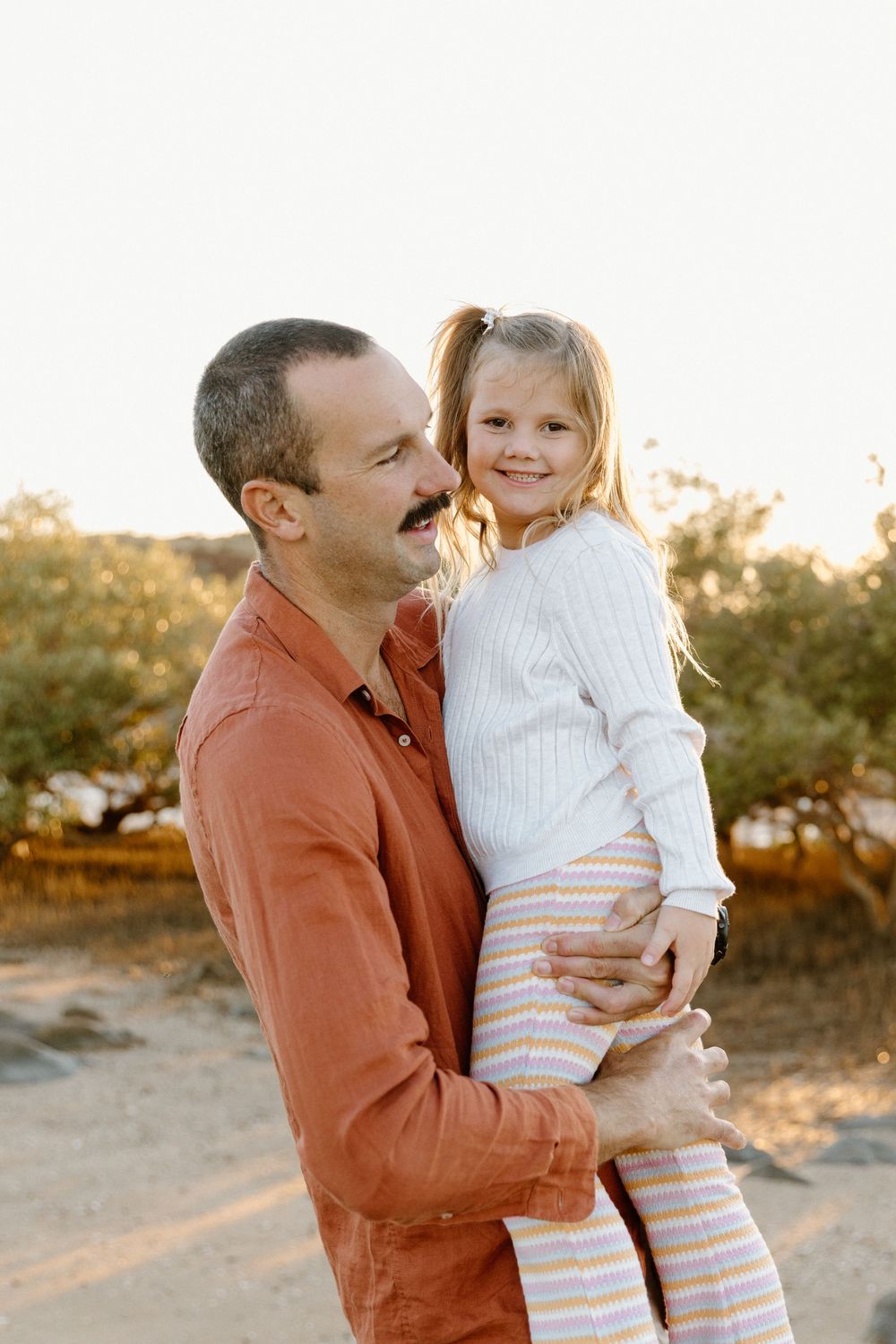 Loving parent and small child share warm embrace outdoors during sunset at a park.