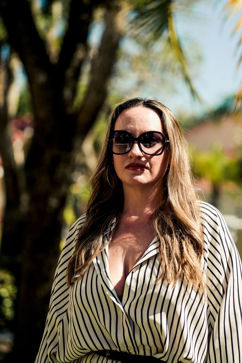 Stylish portrait of a woman in striped shirt and sunglasses outdoors on sunny day.