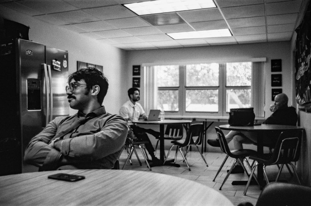 Black and white photo of a classroom with fluorescent lighting and scattered chairs.