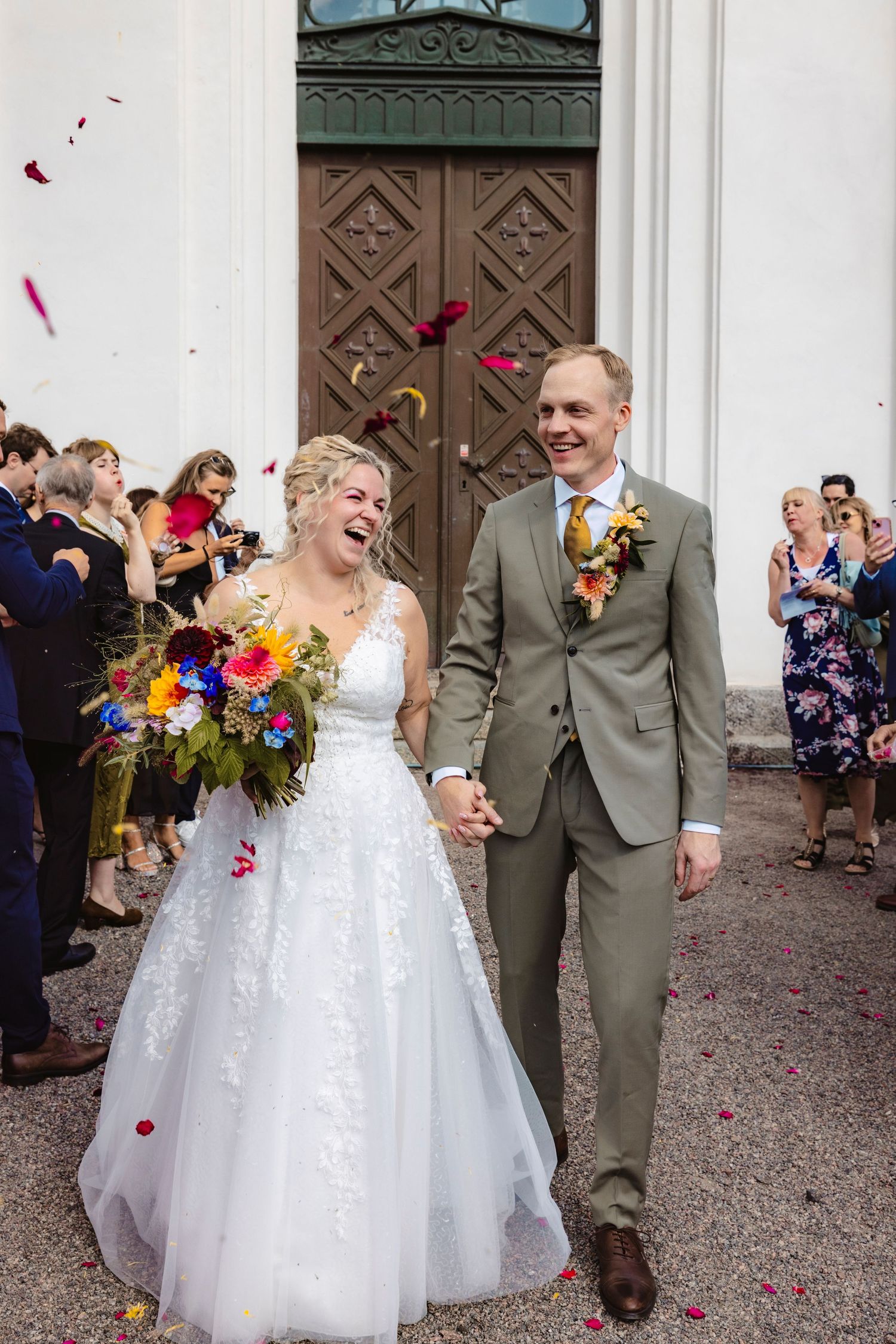 Leende brudpar går från kyrkan medan brölllopsgästerna kastar blomblad över dem.