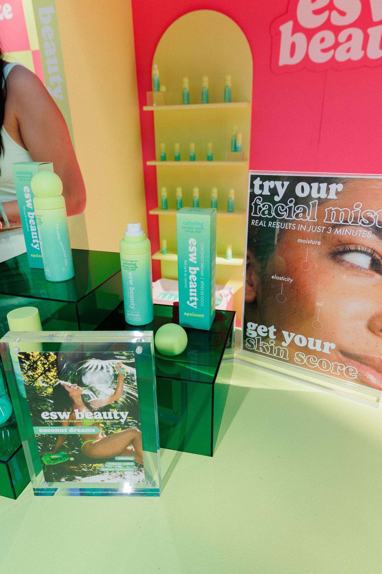 ESW Beauty skincare display with green bottles, facial mist sign, and branded packaging at a beauty pop-up event.