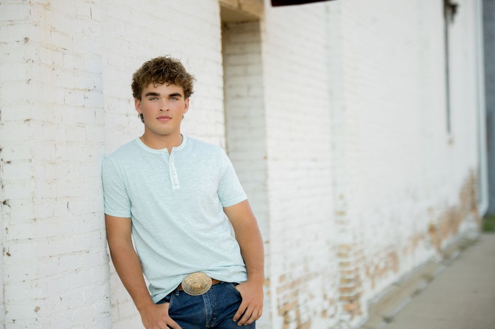 Portrait shot against a white brick wall showing someone wearing a light blue polo shirt and jeans.