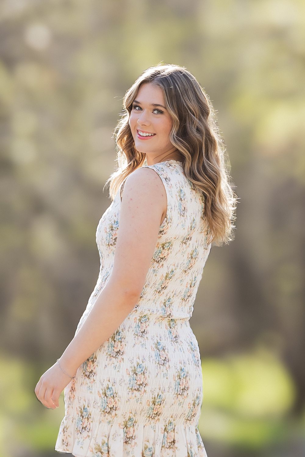 A person in a floral dress poses outdoors with soft natural lighting.