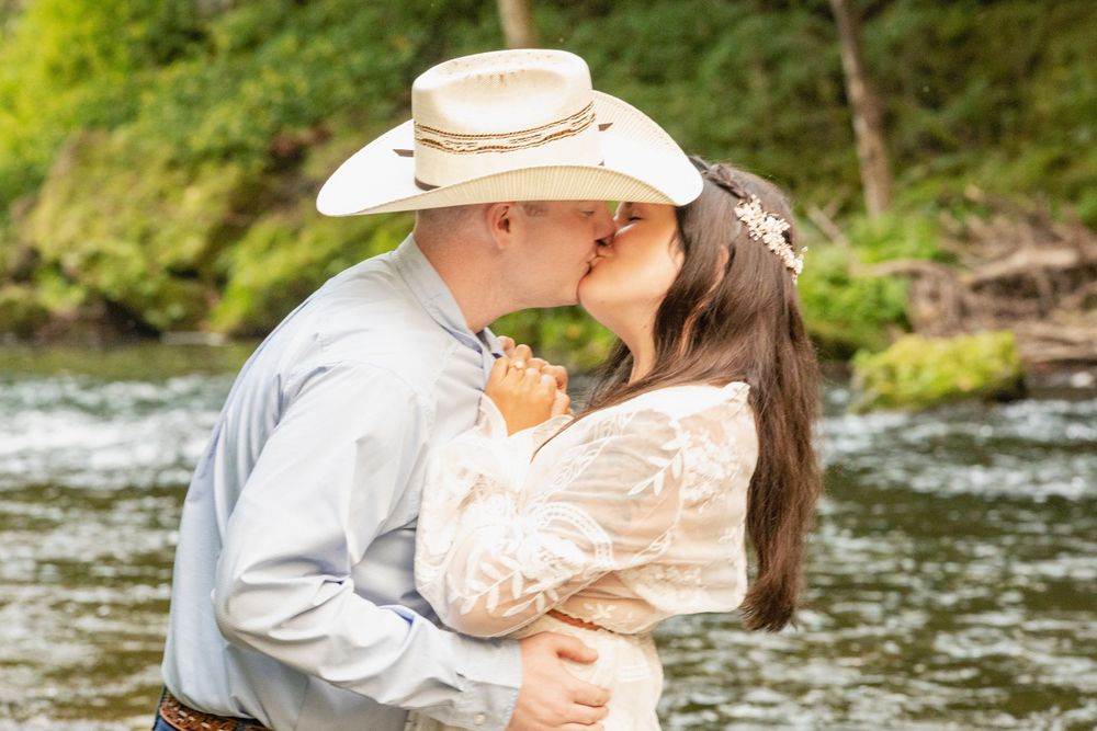 A romantic moment between a couple in western attire by a river.