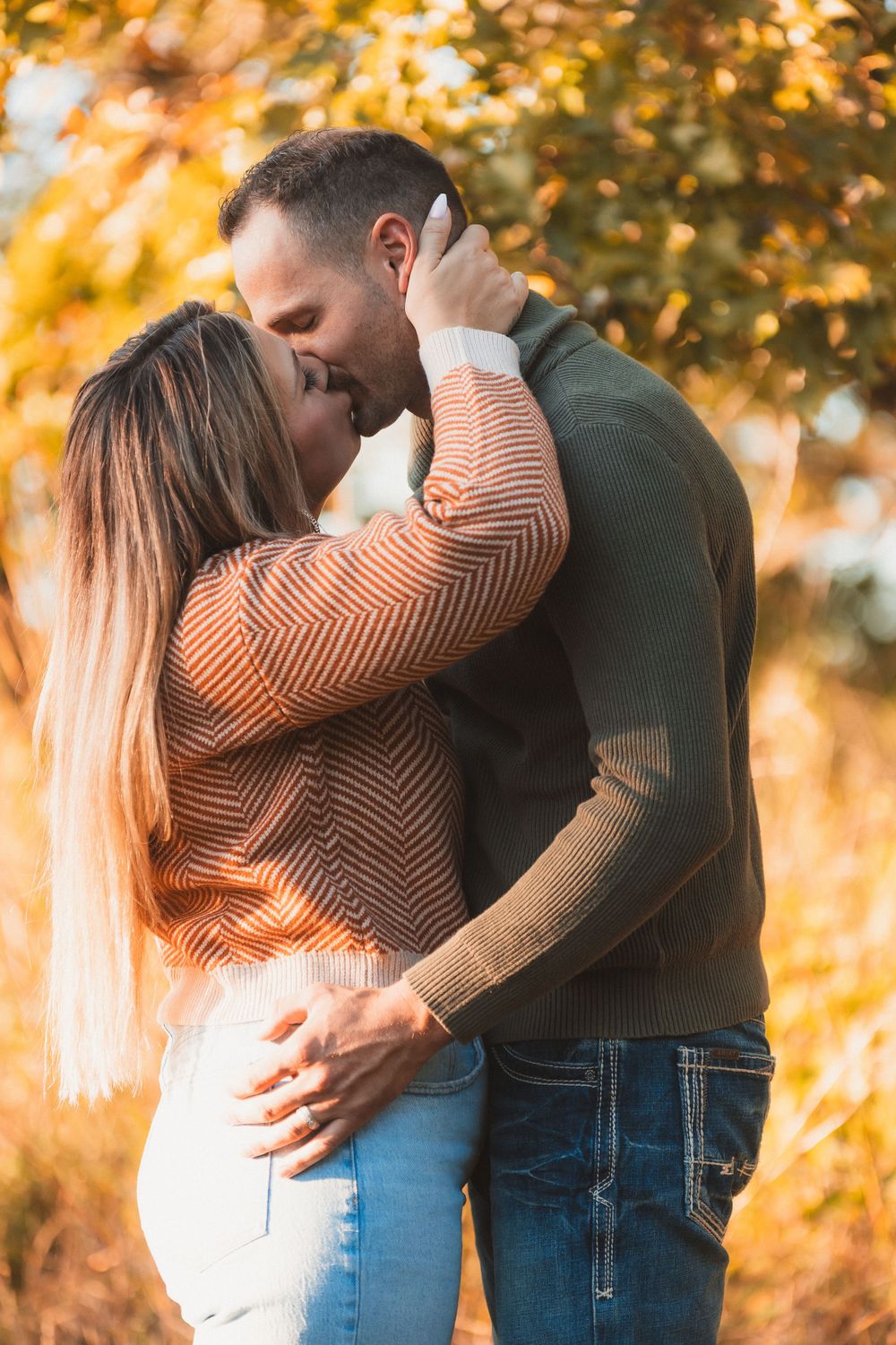 Couple sharing romantic embrace among golden fall foliage.