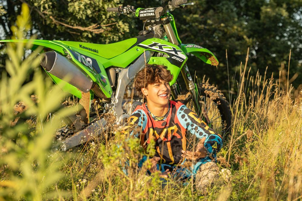 Green dirt bike parked in tall grass during golden hour outdoor photoshoot.