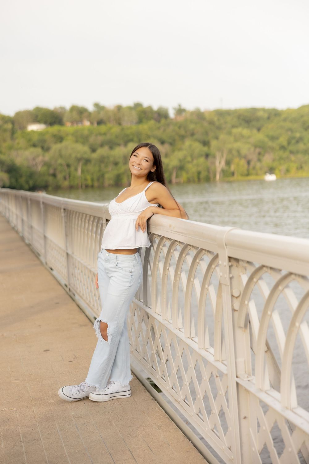 A person poses casually against a decorative bridge railing overlooking a scenic lake during golden hour.