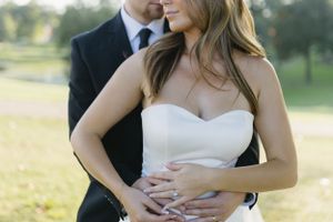 A romantic embrace between a couple in formal attire on a sunny field.