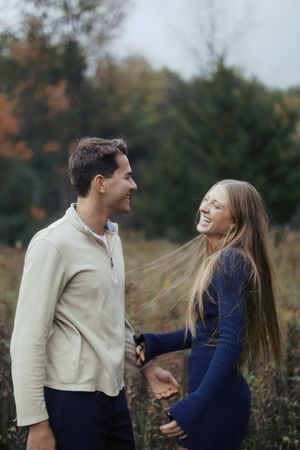 A couple in casual attire share playful moments together in a field during autumn.
