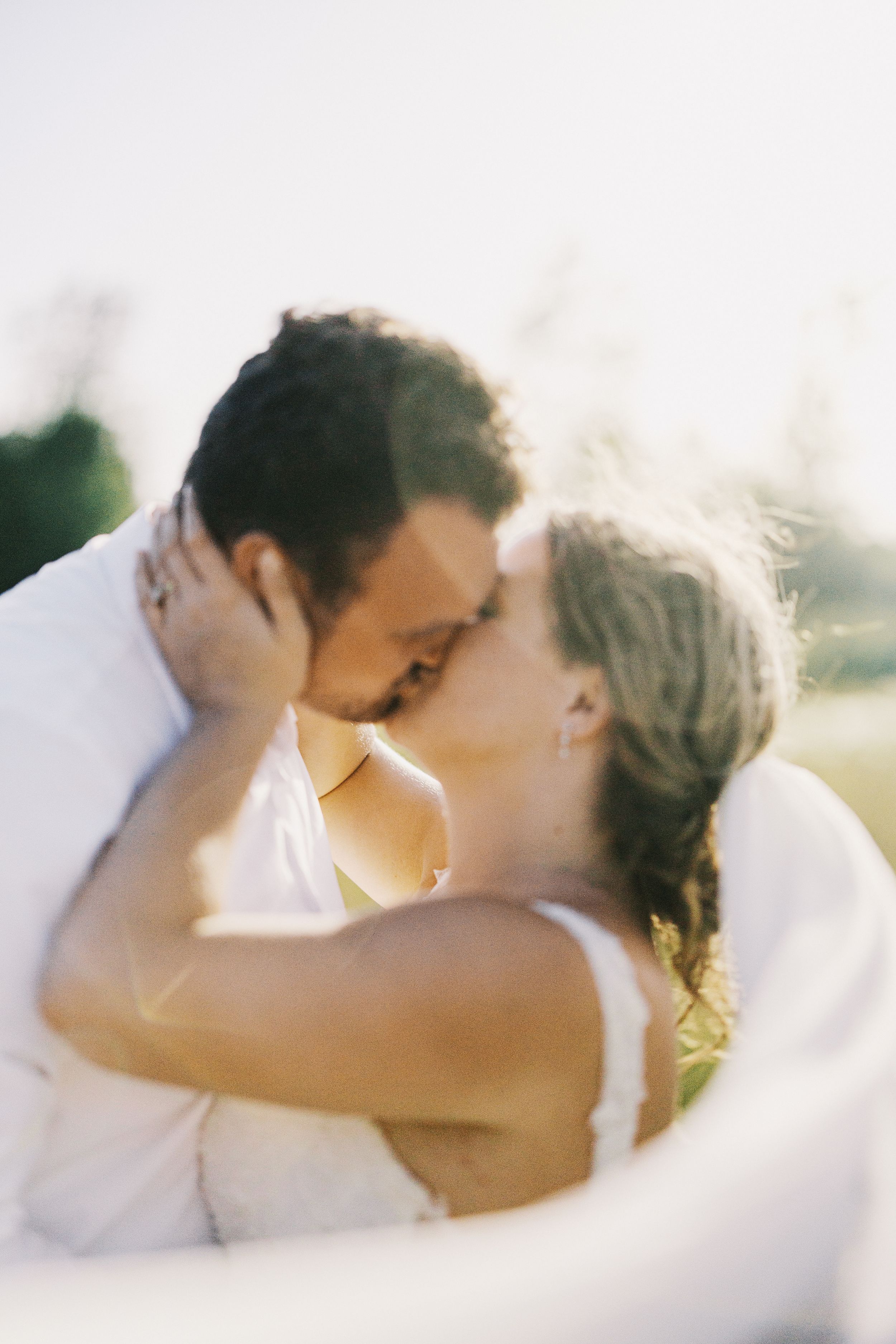 Romantic wedding photo of a couple sharing a tender kiss in soft sunlight.