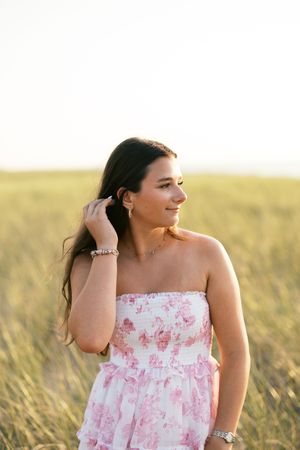 A person in a pink floral dress stands in a sunlit field of tall grass at golden hour.