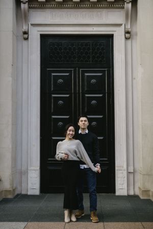 A couple poses playfully in front of a large black ornate door.