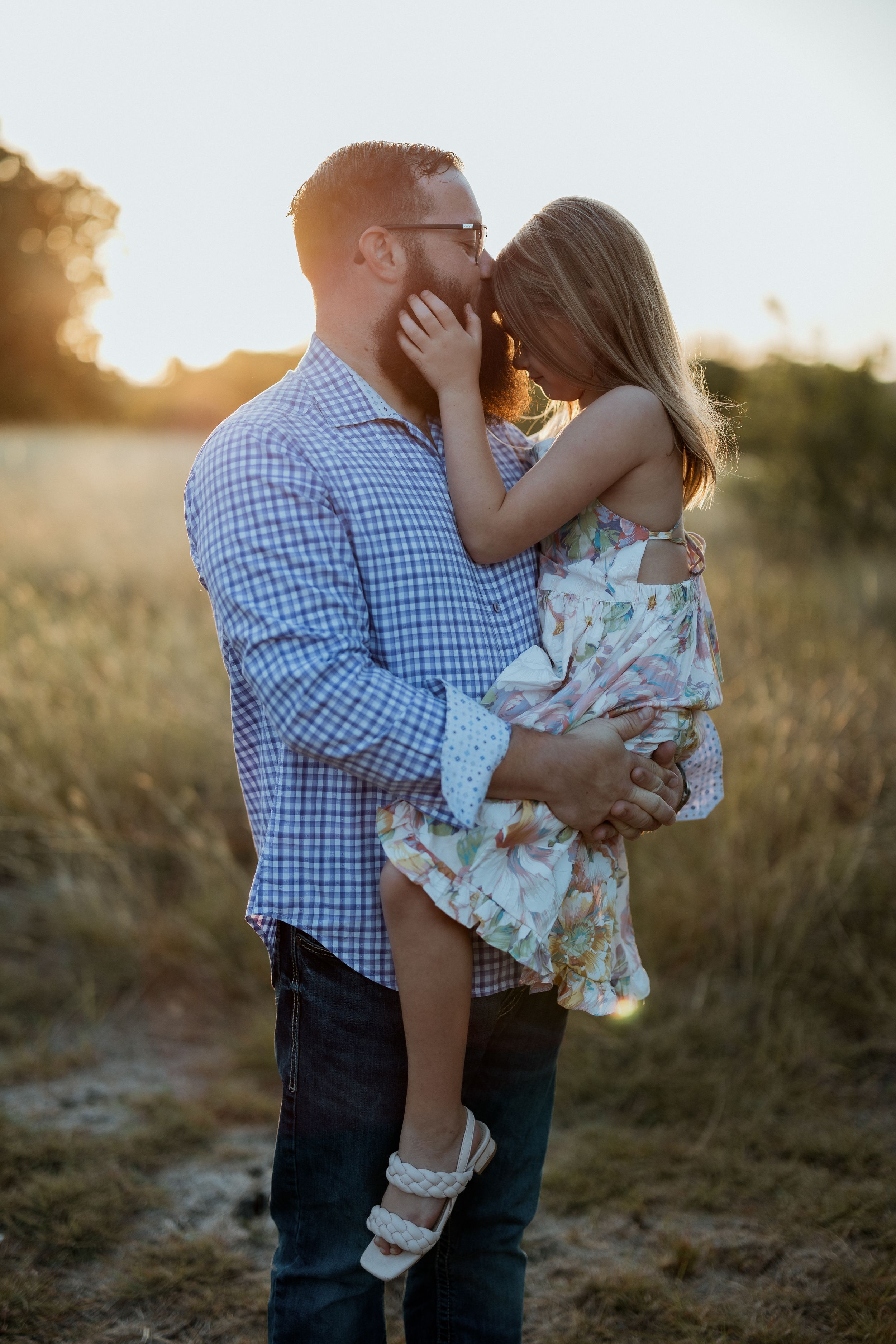 A tender sunset moment captured in a field as a couple embraces during golden hour. Family, Fatherhood, Father and daughter