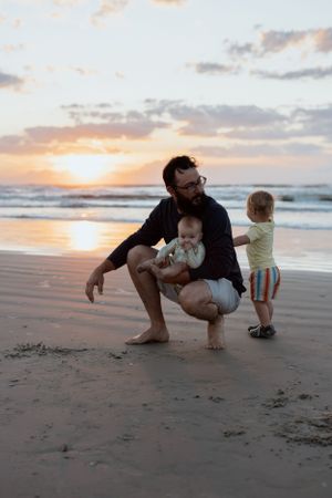 A family enjoys a peaceful moment together on the beach at sunrise as waves roll in along the shoreline. Fatherhood, Father and Children