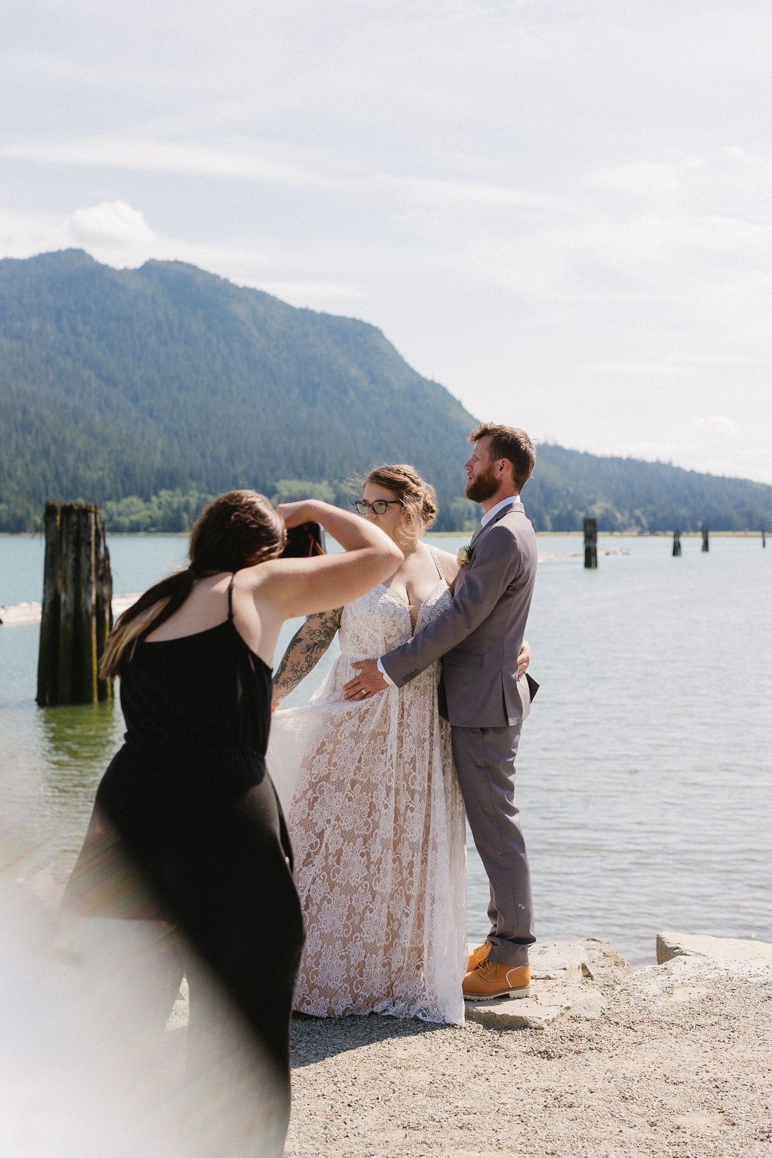 Wedding party helping with dress adjustments by scenic mountain lake.