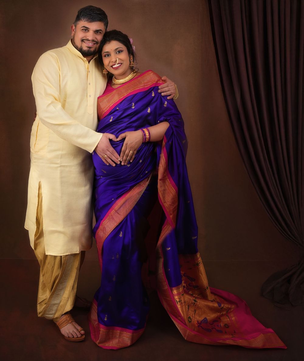 Traditional Indian maternity photoshoot with couple wearing yellow kurta and vibrant blue silk saree against brown backdrop.