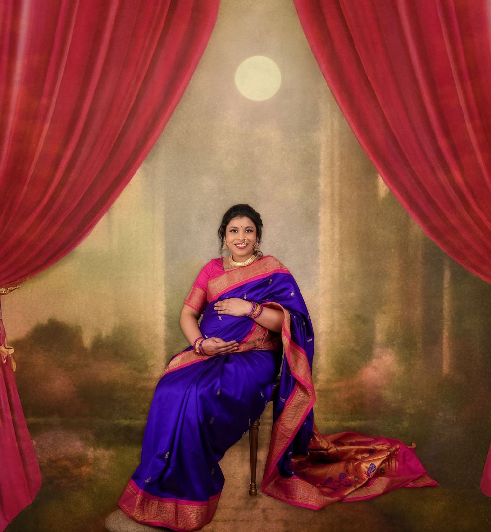 Maternity portrait with bright blue silk saree against dreamy backdrop with red curtains and full moon.