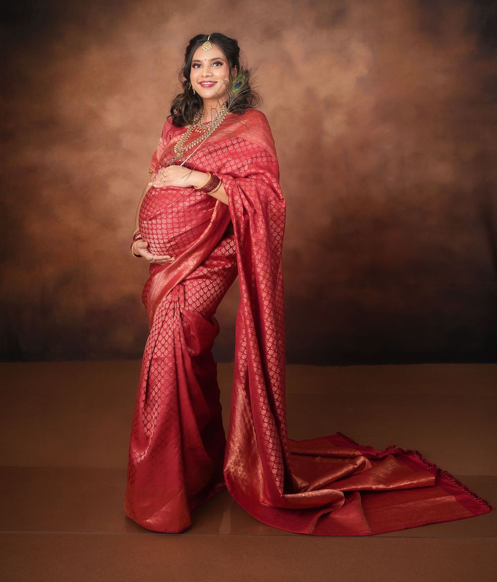 Maternity portrait featuring flowing red silk saree against moody brown backdrop.