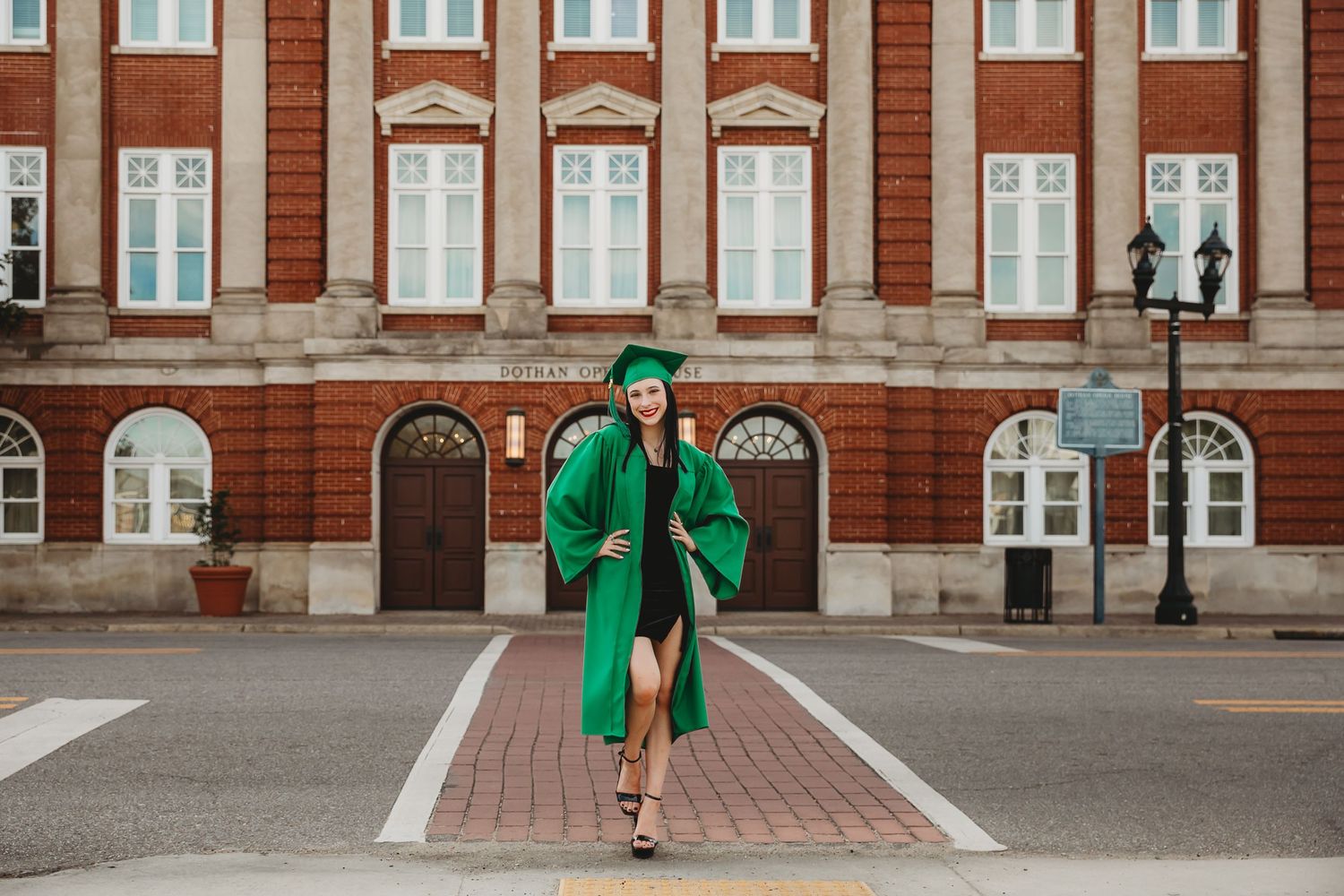 A person in a bright green graduation gown walks confidently across a brick courtyard in front of a classic building.