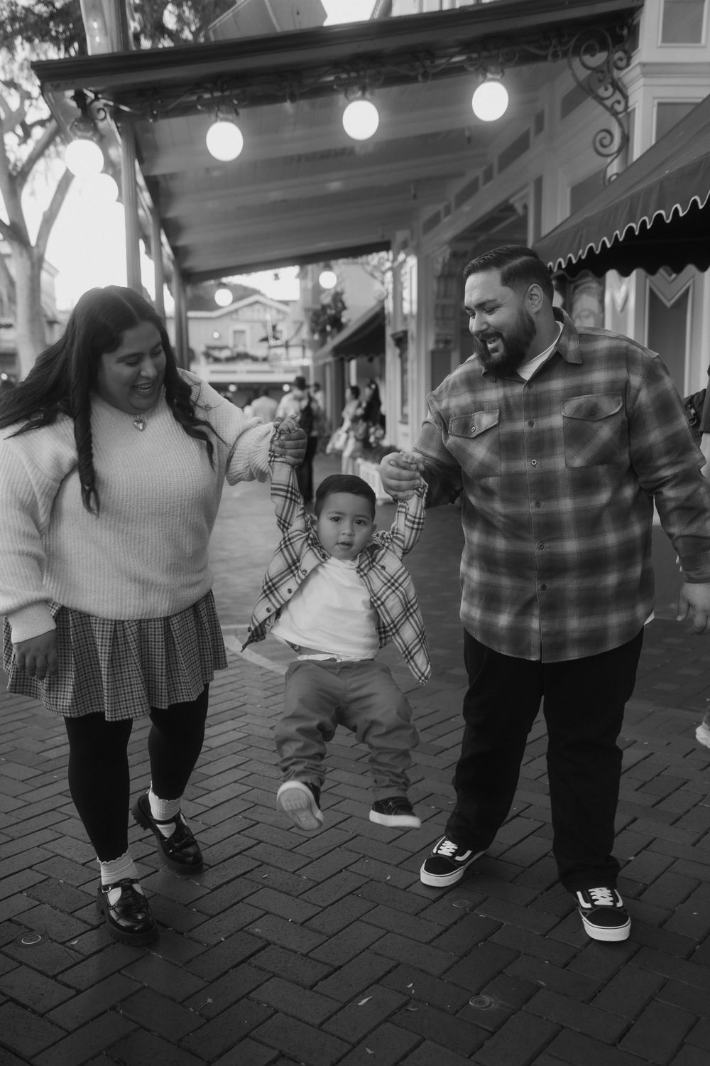 A joyful moment on a brick walkway as a toddler jumps while holding hands with others.
