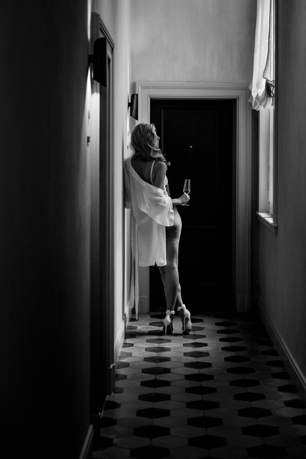 Silhouette in hallway wearing white robe and heels against checkered floor.